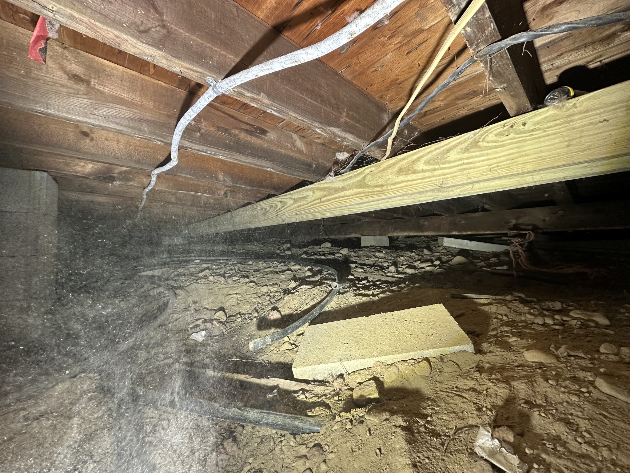 Crawlspace floor cleared of contaminated insulation — exposed joists, wiring, and soil documented mid-remediation prior to soil treatment