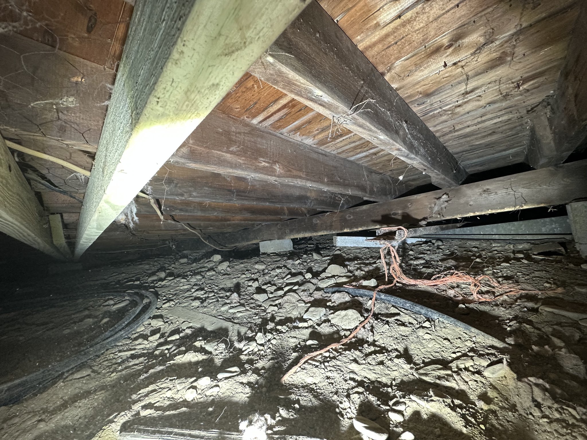 Wide-angle view of cleared crawlspace — floor joists exposed, debris removed, foundation piers visible, full extent of space documented