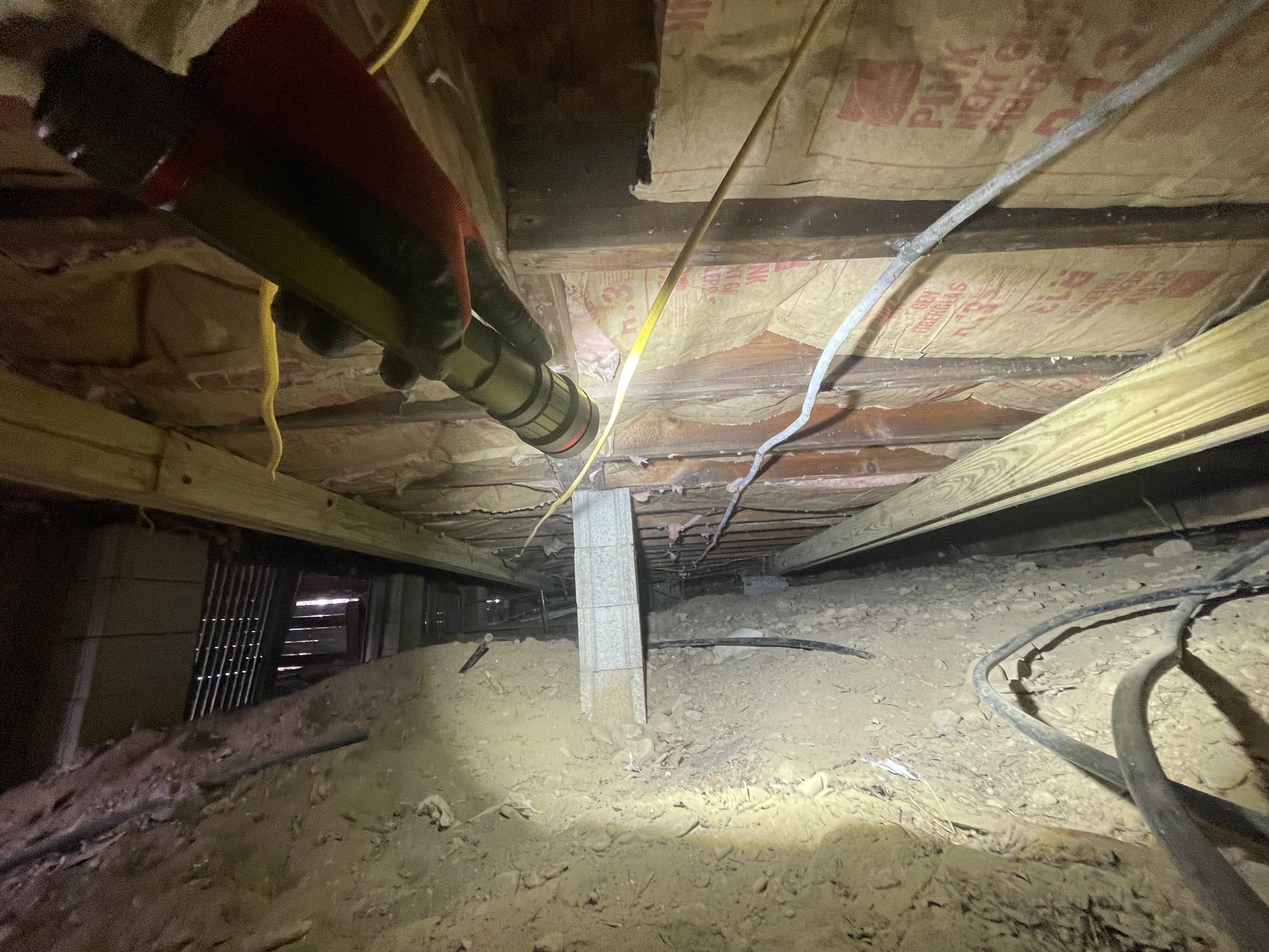 Wide-angle view of cleared crawlspace — foundation pier, vent opening, and full floor span documented after complete insulation and debris removal